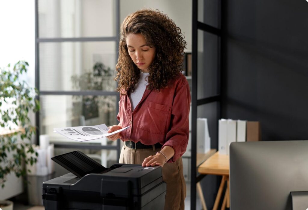 Woman getting pages from printer in modern office
