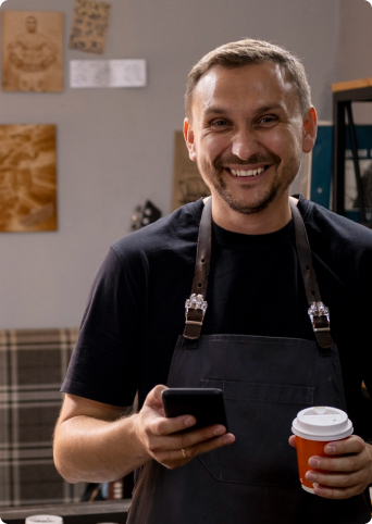 Man smiling and while holding his phone and coffee